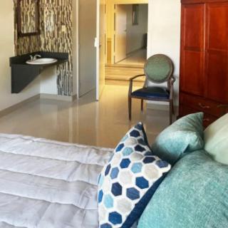 A modern bedroom featuring stylish decor with patterned pillows, a chair, and a visible sink area.