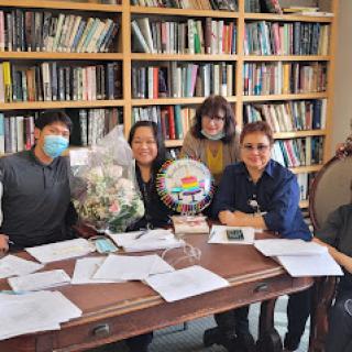 A group of individuals celebrating with flowers and a decorative plate in an office setting surrounded by books.
