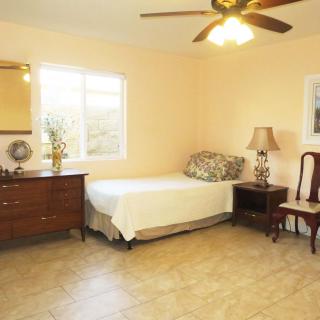 A cozy bedroom featuring a single bed, a dresser with a mirror, a lamp on a side table, and a comfortable chair.
