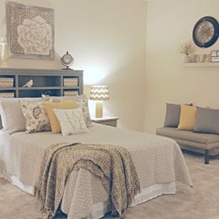 A cozy bedroom with neutral-toned decor, featuring a bed with multiple pillows and a stylish lamp.