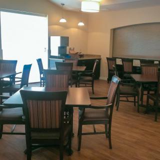 An empty dining area with wooden tables and chairs, featuring a bar section in the background.