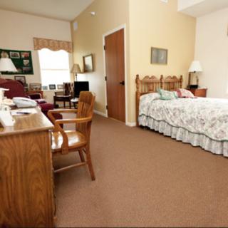 A cozy bedroom with a wooden bed, desk, and chair, featuring warm lighting and homey decor.