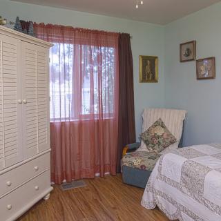 Cozy bedroom with classic armoire, bed, and a comfortable chair next to a window with sheer curtains.