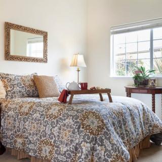 A cozy bedroom with a patterned bedspread, bedside lamp, and a window letting in natural light.