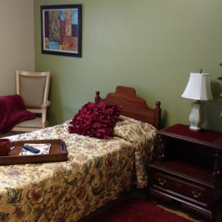 A cozy bedroom with a single bed, nightstand with a lamp, and a painting on the wall.