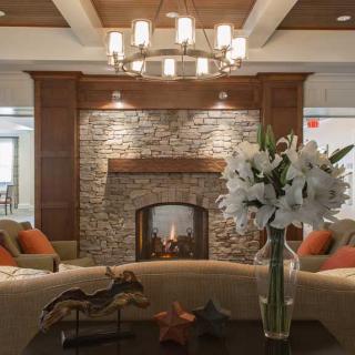 A cozy living room with a brick fireplace, elegant chandelier, and floral decoration.