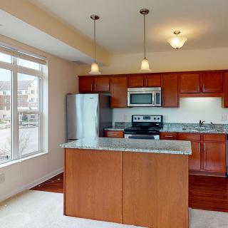 A modern kitchen featuring stainless steel appliances, wooden cabinetry, and a central countertop island with pendant lighting.