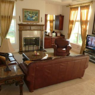 A cozy living room with a leather sofa, armchair, and fireplace, complemented by large windows and classic furnishings.