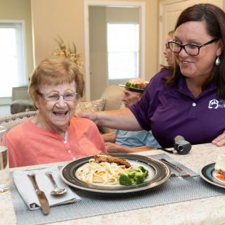 A caregiver assisting a senior woman during mealtime at an assisted living facility.