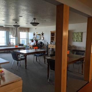 A quiet room with several tables and chairs, adorned with artwork and large windows.
