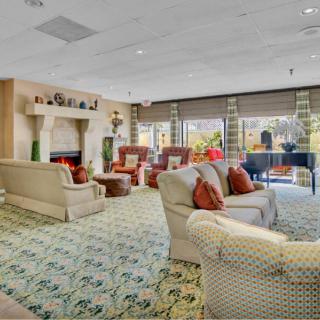 A spacious lounge with comfortable sofas, a fireplace, and a grand piano by large windows.