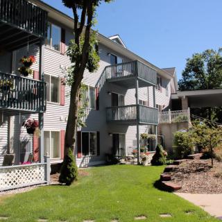 A view of an apartment building with multiple balconies, surrounded by landscaped grounds on a sunny day.