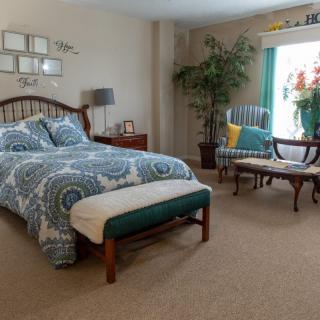 A cozy and well-decorated bedroom with a large bed, stylish armchair by the window, and indoor plants.