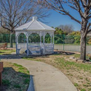 A serene park setting featuring a white gazebo surrounded by trees and a pathway.