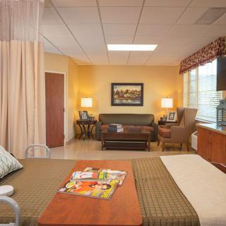 A well-furnished hospital room featuring a bed, sofa, and a window with natural light.
