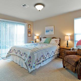 A cozy bedroom with a neatly made bed, two bedside lamps, and a comfortable chair by the window.