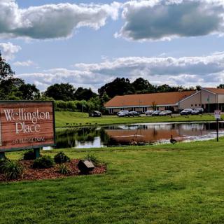 A scenic view of a park with a pond, sign, and buildings in the background under a cloudy sky.