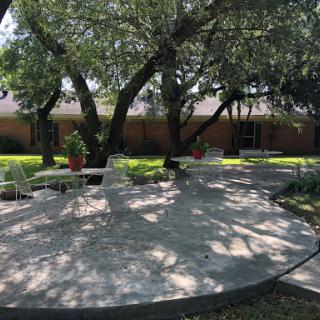 A serene outdoor space featuring shaded seating under large trees.