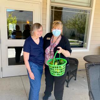 Two individuals standing outside a building, one holding a green basket.