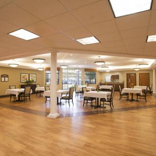 A spacious and thoughtfully designed dining area with tables set for guests, featuring warm lighting and wooden flooring.