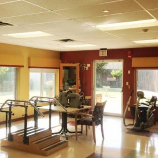 A therapy room in a rehabilitation center equipped with exercise equipment, including treadmills and seating areas for elderly care.