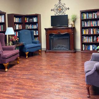 A cozy library room with bookshelves, armchairs, a fireplace, and a television.