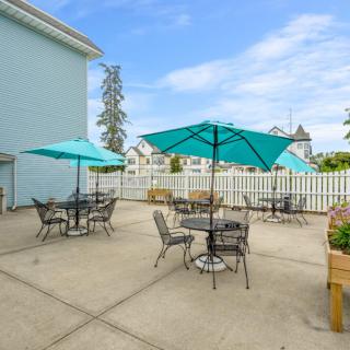 A sunny outdoor patio with tables, chairs, and teal umbrellas surrounded by a white fence.