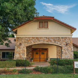 A charming house with a stone facade and wooden doors, surrounded by greenery.