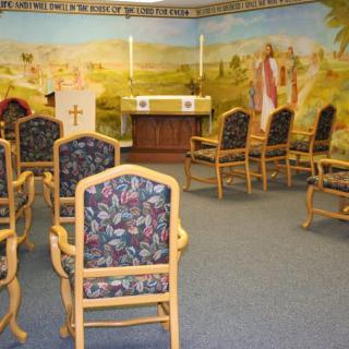 A small chapel with a mural, featuring an altar and arranged chairs.