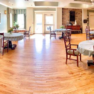 A bright and spacious dining room with wooden floors, featuring round tables and chairs.