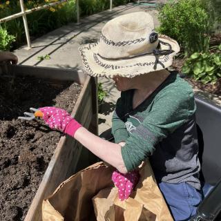 A person gardening outdoors, wearing a hat and gloves while working with soil.