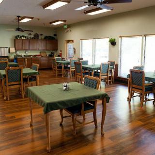 A spacious dining area with multiple tables and chairs, featuring green tablecloths and wooden flooring.