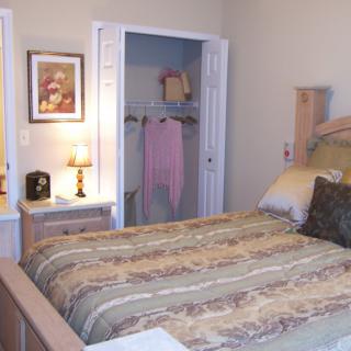 A cozy bedroom with a neatly made bed, an open closet, and a small lamp on the nightstand.