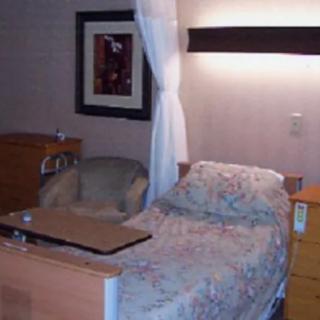 A hospital room with a bed, side table, chair, and wall art.