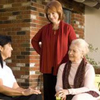 Three elderly women engaged in conversation outside near a brick wall.