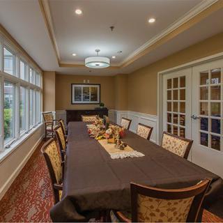 A well-appointed dining room with a long table set for a meeting or meal, featuring elegant decor and ample natural light from large windows.