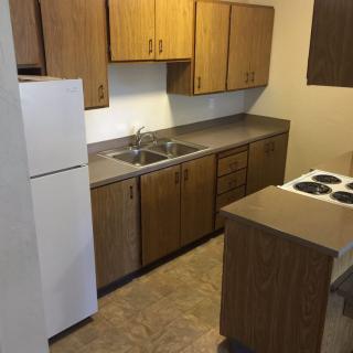 A small apartment kitchen with wooden cabinets, a stove, and a refrigerator.