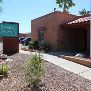 A brick building with a sign reading 'Sabino Canyon' surrounded by desert landscaping and palm trees.