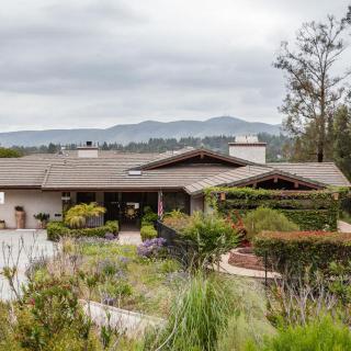 A modern house surrounded by a lush garden with mountains in the background.