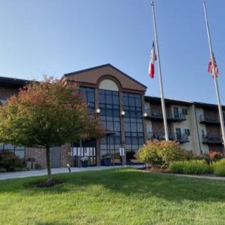 A modern building with a glass facade, surrounded by trees and flags, under a clear blue sky.