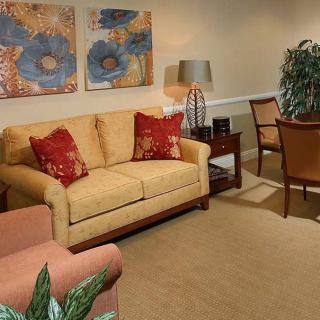 A cozy living room with a beige sofa, red pillows, artwork on the wall, and a lamp beside a green indoor plant.