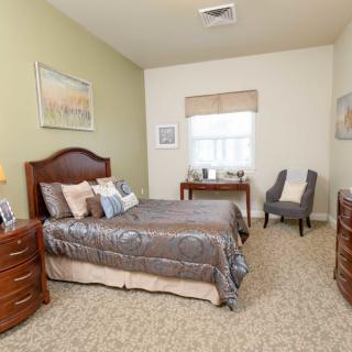 A cozy bedroom with a bed, nightstands, dresser, and a chair by the window.