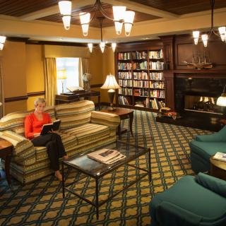 A cozy library room with a person reading on a couch, surrounded by bookshelves and a fireplace.