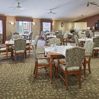 A spacious dining area with multiple set tables and chairs, ceiling fans, and a carpeted floor.