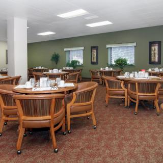 An empty dining room with multiple round tables and wooden chairs.