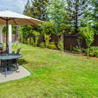A serene backyard with a patio set under an umbrella, surrounded by a lush green lawn and trees.