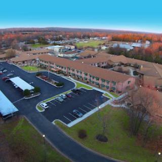 Aerial view of a hotel surrounded by autumn foliage and a spacious parking lot.