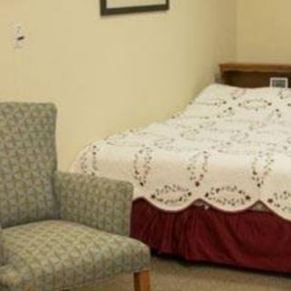A cozy bedroom with a neatly made bed and an upholstered chair.