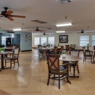An empty dining room with neatly arranged tables and chairs, featuring wooden floors and ceiling fans.