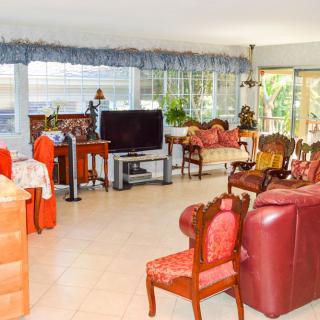 A spacious living room with various furniture pieces, including sofas, chairs, and a television, bathed in natural light from large windows.